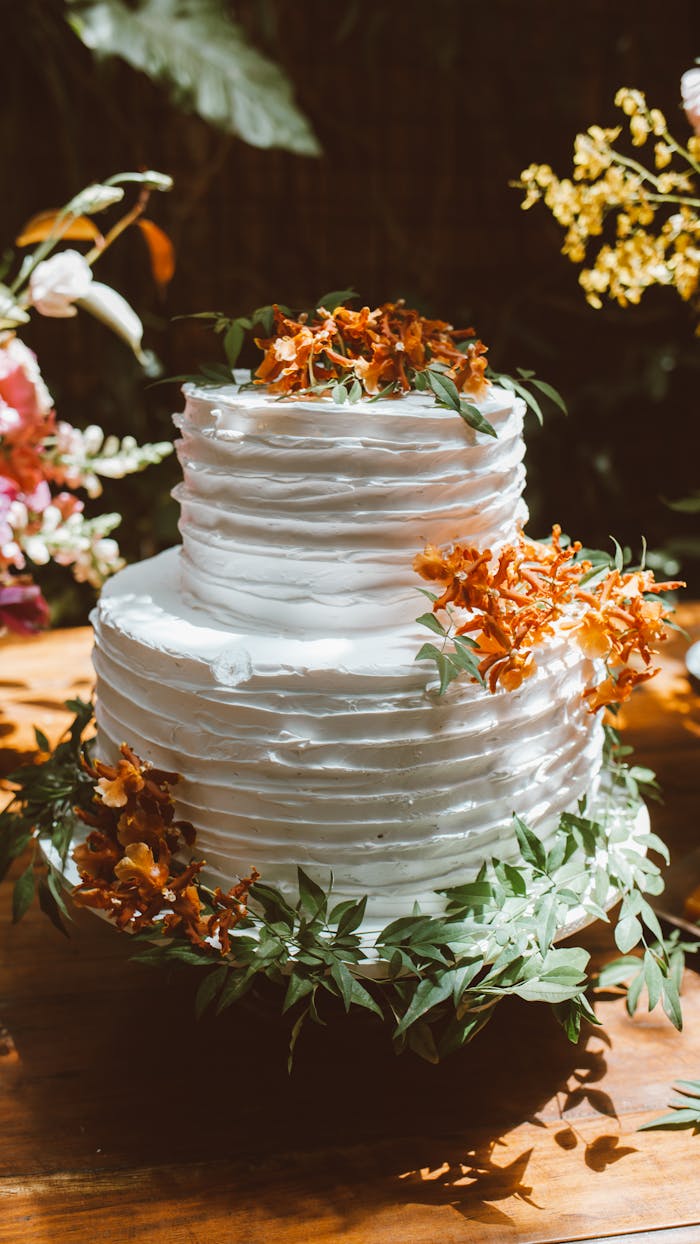 A beautifully decorated white wedding cake adorned with vibrant flowers and greenery, perfect for a summer celebration.