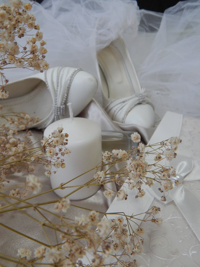 A delicate arrangement featuring white bridal heels, candles, and dried flowers in a soft, romantic setting.
