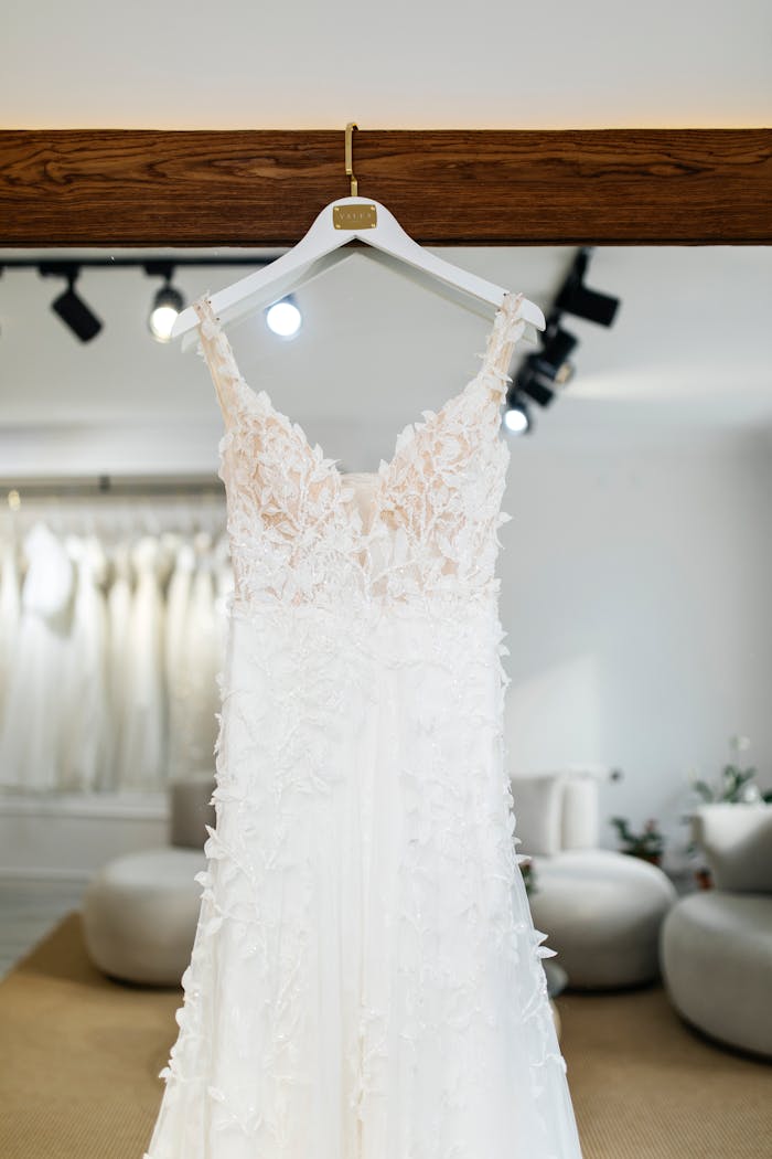 A delicate lace wedding dress on a hanger in an elegant bridal shop setting.