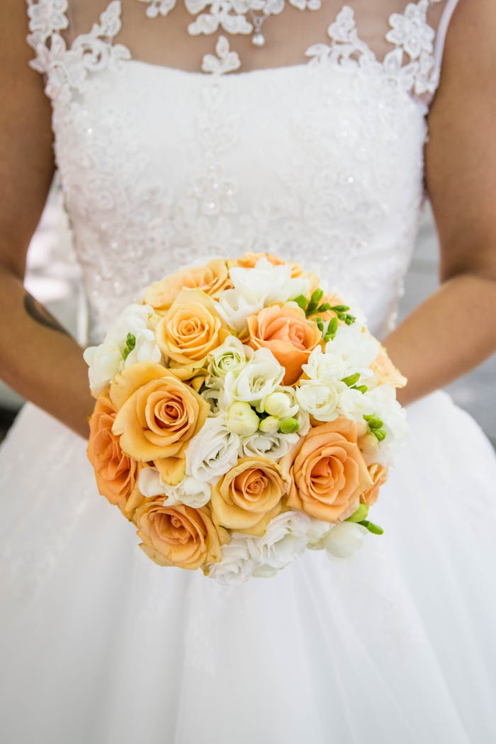 gallery-6 A bride holding an elegant bouquet of peach and white roses, ready for the wedding ceremony.